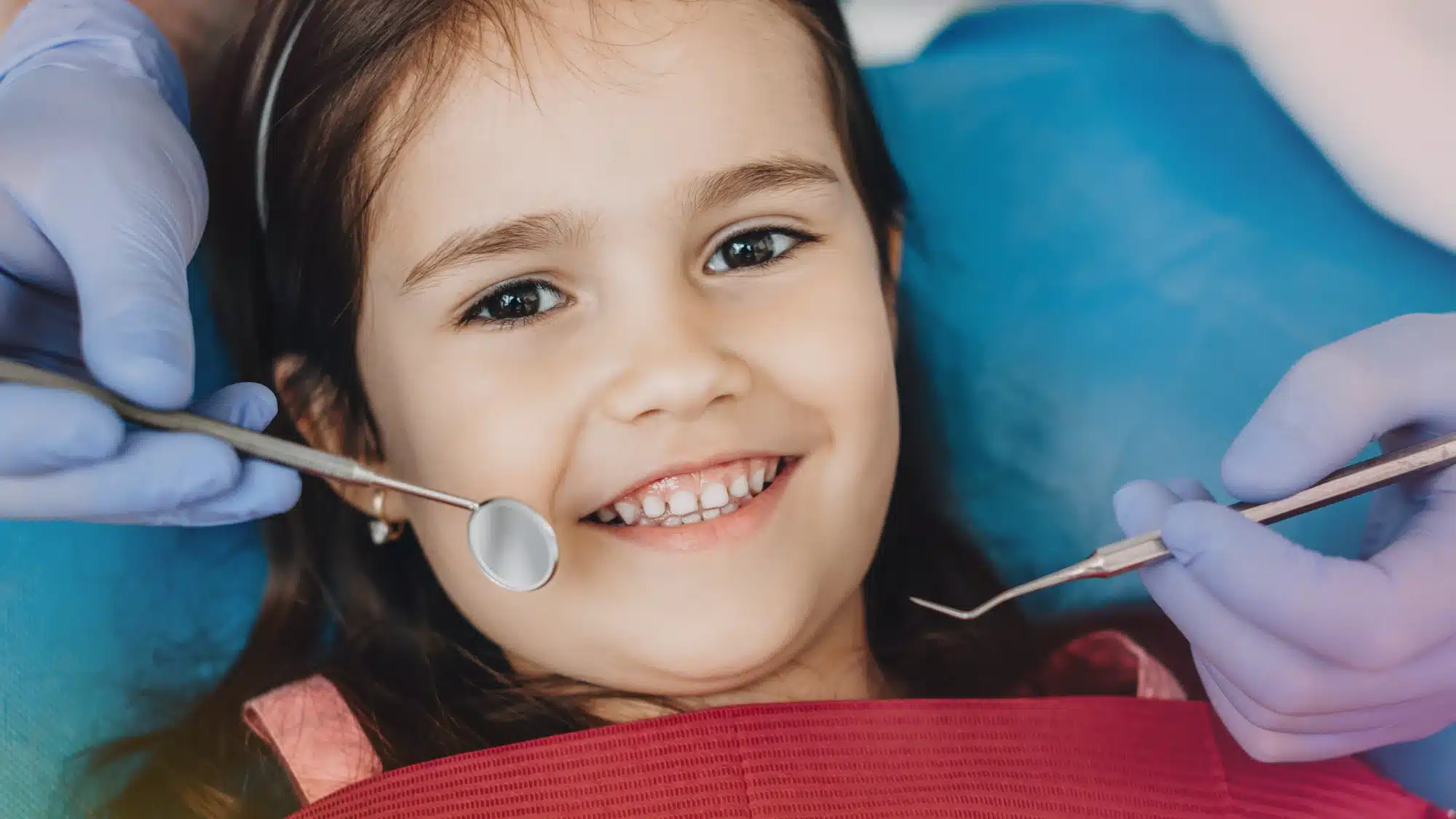 Pediatric dentist examining child’s teeth in dental clinic while parent observes during preventive dental care visit