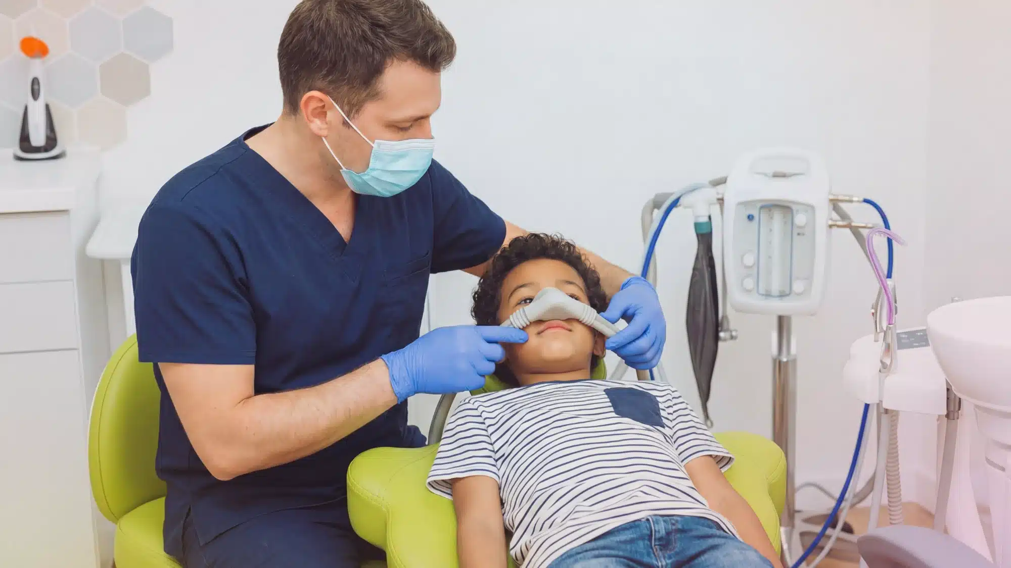 Pediatric dentist using sedation dentistry techniques while child patient receives dental treatment in a calm clinic environment