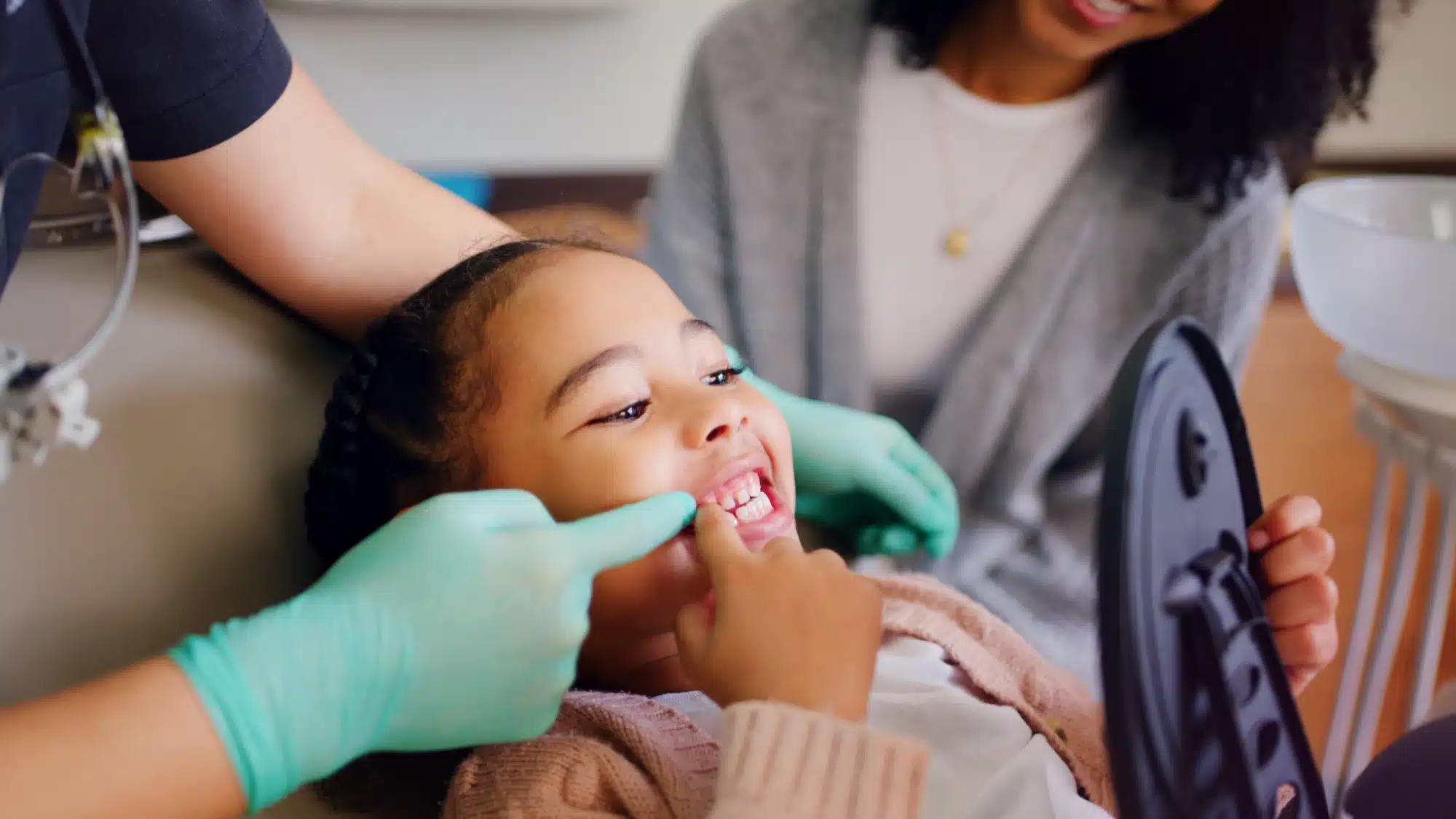Pediatric dentist gently examining child’s teeth while explaining oral care differences compared to adult dental treatment